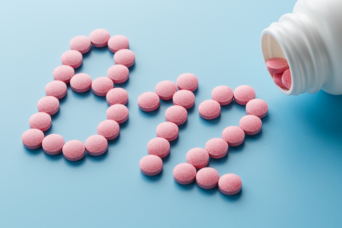 Pink Vitamins in the shape of the letter B 12 on a blue background, spilled from a white can. Food supplement concept