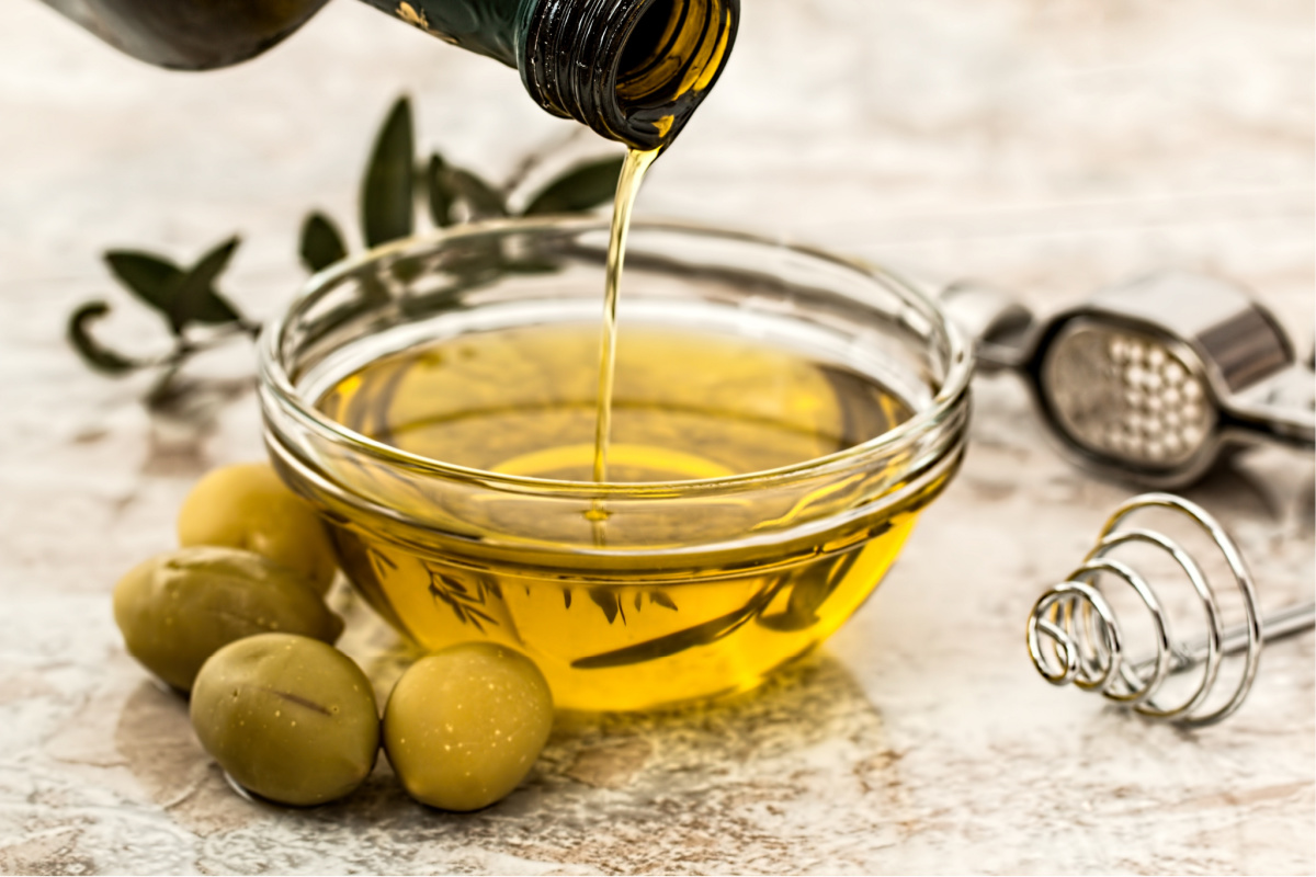 Unidentified person pouring olive oil into a glass dish - oil is another vegan supermarket essential