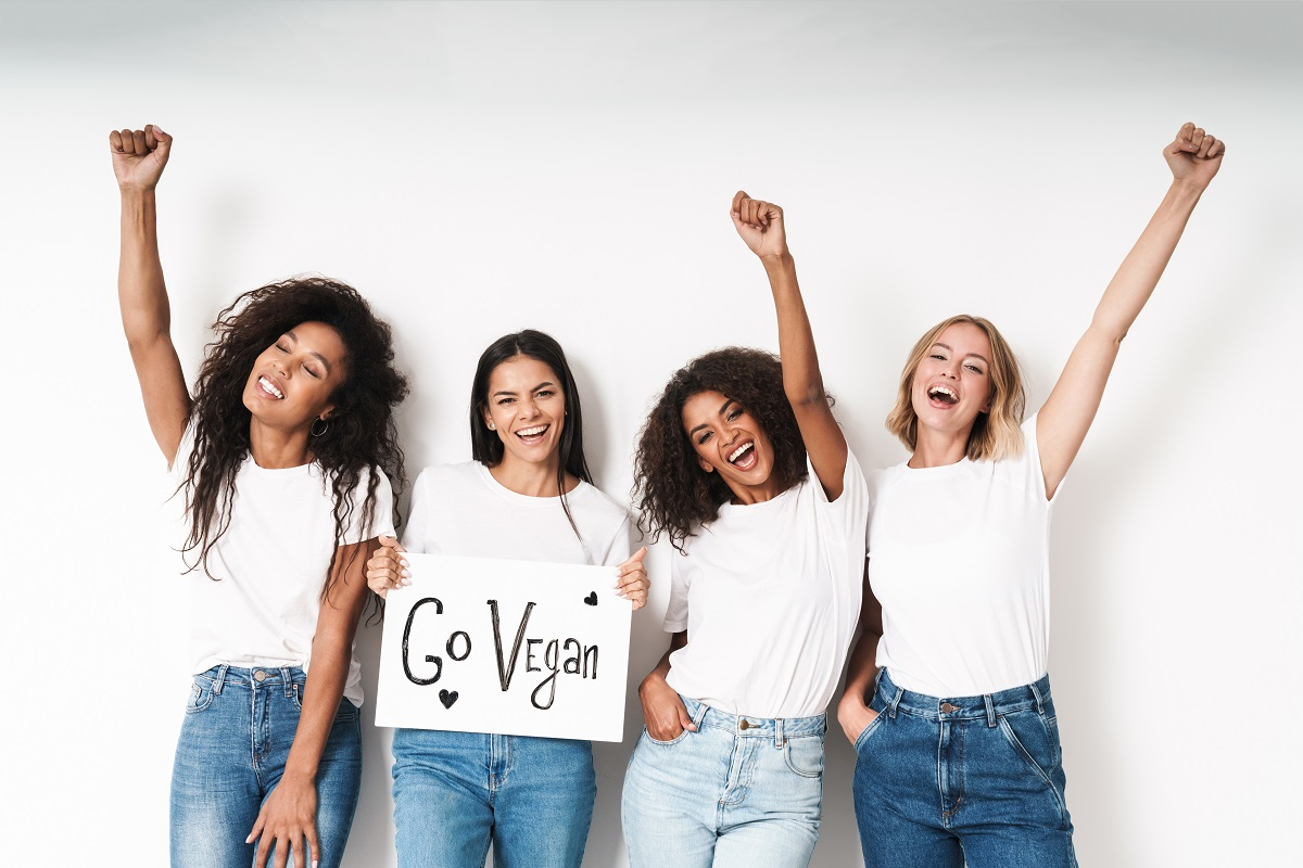 4 women cheering, holding a "Go Vegan" sign.