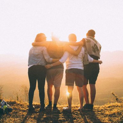 A group of people standing on a hill with their arms linked around one another 