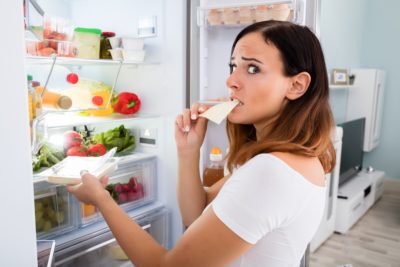 Woman Eating Cheese In Front Of Refrigerator