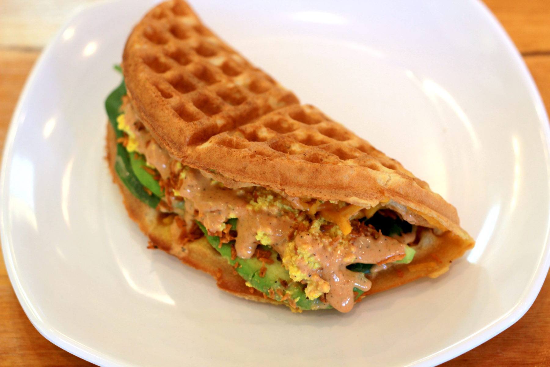 TIABI's The Spicy Vegan shows a "wafflewich" with tofu scramble, avocado, vegan bacon, and aioli tucked inside a folded waffle 