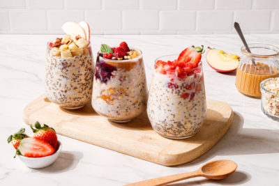 Three jars of overnight oats with strawberry, apple, and cherry toppings sit on a wooden cutting board