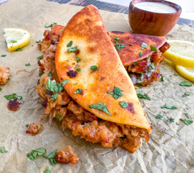 A pile of vegan crab cake tacos is garnished with cilantro and lemon sices