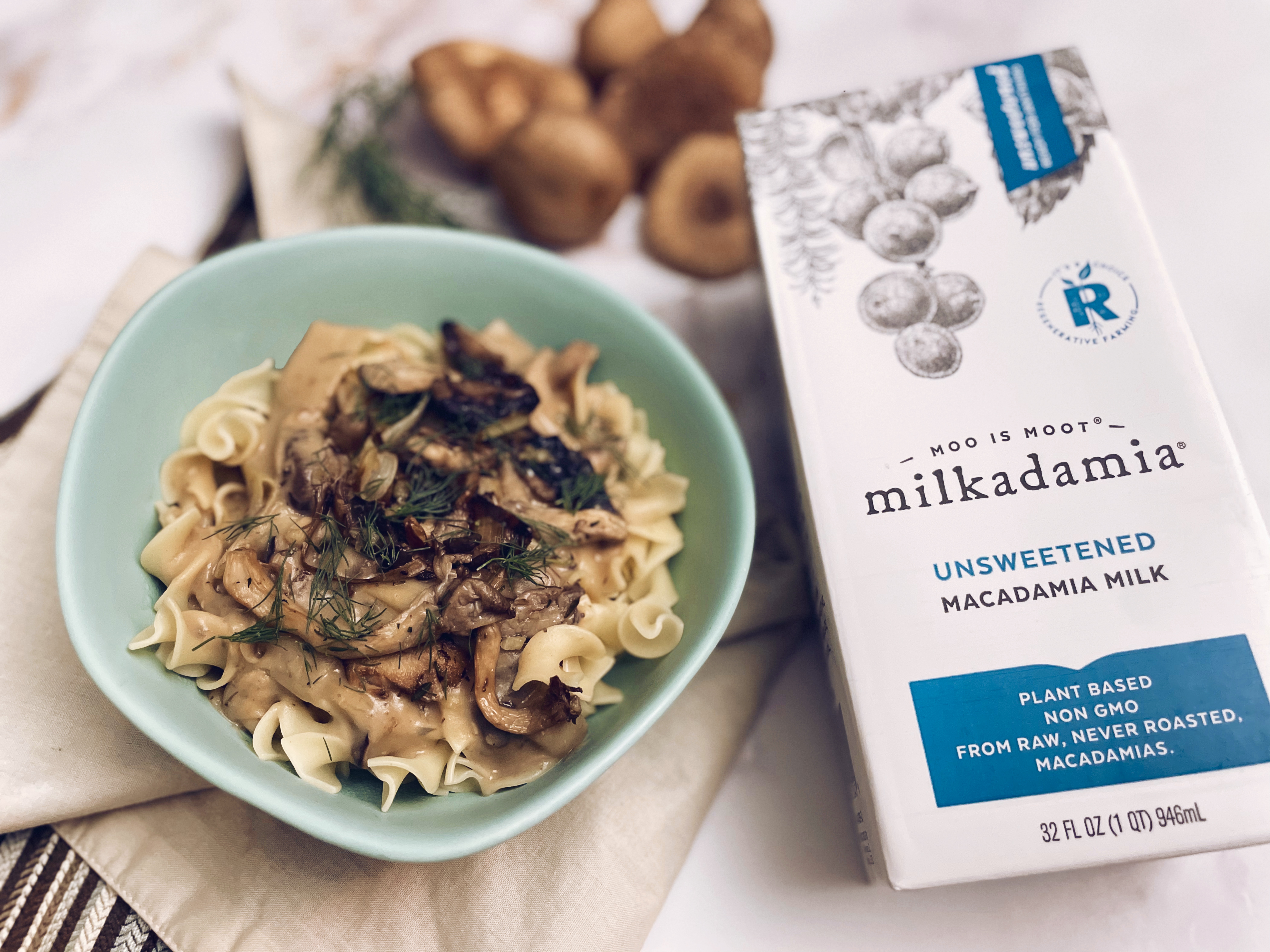 A bowl of vegan mushroom stroganoff next to a carton of Milkadamia milk