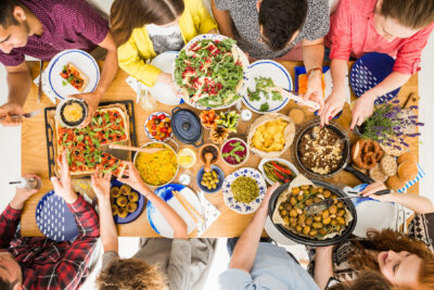 Delicious vegan dinner, top view of communal table and friends sitting together and sharing a vegetable meal