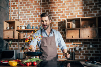 stylish young man with apron frying vegetables